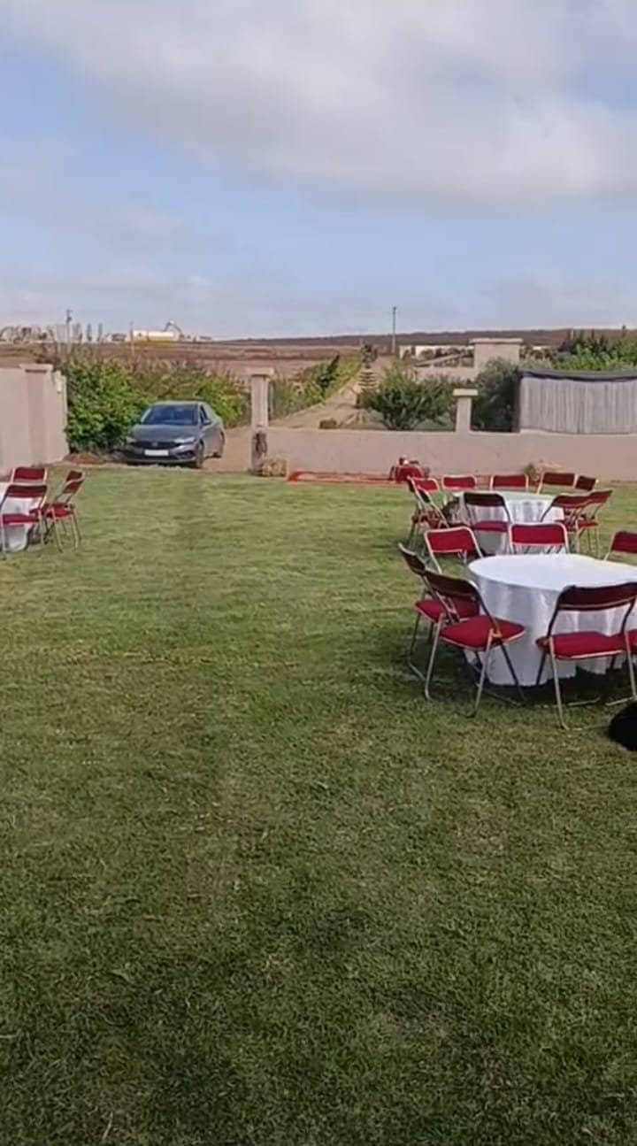 La pelouse dressée pour une fête : tables rondes et chaises face aux champs